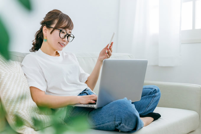 パソコンとスマートフォンで在宅ワークをする女性