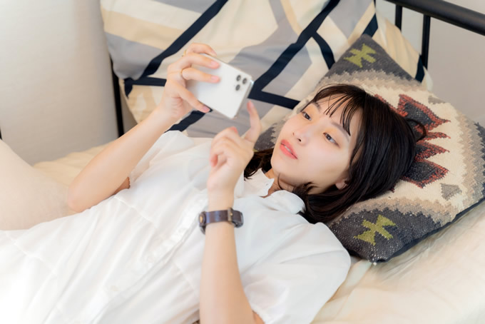 寝転びながらスマートフォンを操作する女性